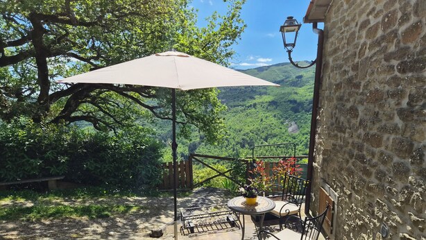 A patio with a table and chairs, a hanging lantern, and a view of a lush valley. - Charming Tuscan apartment with a pool, views, and a private terrace (Toscana)