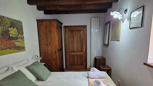 A bedroom with a bed, pillows, a wooden wardrobe, a radiator, a small table, and a wall-mounted light fixture. - Charming Tuscan apartment with a pool, views, and a private terrace (Toscana)