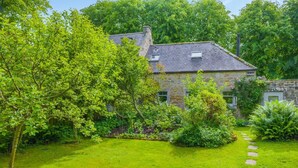 Una casa in pietra con un giardino, un vialetto in pietra e un albero grande.