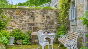 Un muro in pietra, un tavolo con sedie e una panchina in un giardino.