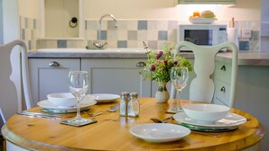 Un tavolo da pranzo apparecchiato con piatti, ciotole, bicchieri da vino e condimento, in una cucina con zanzariera a scacchi e un forno a microonde.