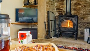 Ein gemütliches Wohnzimmer mit Kamin aus Stein, einem Fernseher und einem Tisch mit Gebäck.