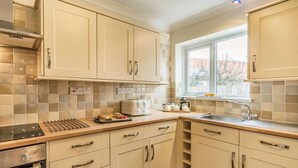 A kitchen with white cabinets, a window, a sink, and a countertop with a kettle and teapot. - 4 Bed in Beadnell (oc-cn167) (Beadnell)