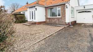 A two-story house with a tiled roof, a front garage, and a gravel driveway. - 4 Bed in Beadnell (oc-cn167) (Beadnell)
