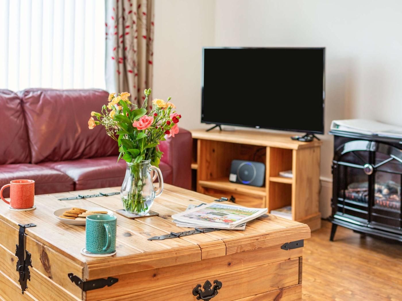 Una sala de estar con una mesa de centro de madera, un jarrón con flores, un televisor y un sofá.