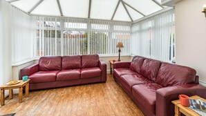 A conservatory with two leather sofas, a wooden table, and a lamp. - 4 Bed in Beadnell (oc-cn167) (Beadnell)