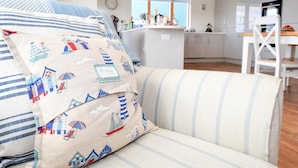 Ein modernes Wohnzimmer mit gestreiftem Sofa, eine Küche im Hintergrund und Blick ins Freie.