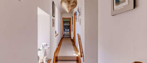 A hallway with a wooden staircase, a hanging light fixture, and framed artwork on the walls.