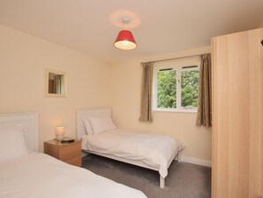 A bedroom with two beds, a bedside table with a lamp, a window with curtains, and a red ceiling light. - 3 Bed in Rowlands Gill (oc-cn209) (Rowlands Gill)