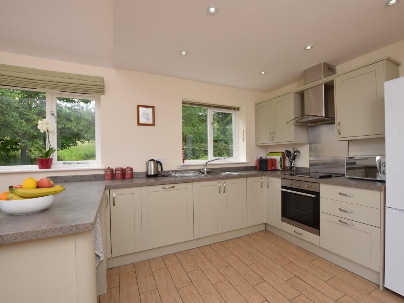 A modern kitchen with a large island, built-in oven, and a view of greenery outside.