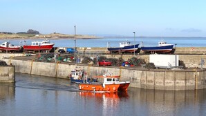A harbor with several boats docked, a concrete breakwater, and a distant castle on the horizon. - 2 Bed in Seahouses (oc-cn220) (Seahouses)