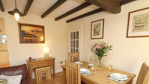 A dining area with a wooden table set for two, a brown leather sofa, and a small desk with a lamp. - 2 Bed in Seahouses (oc-cn220) (Seahouses)
