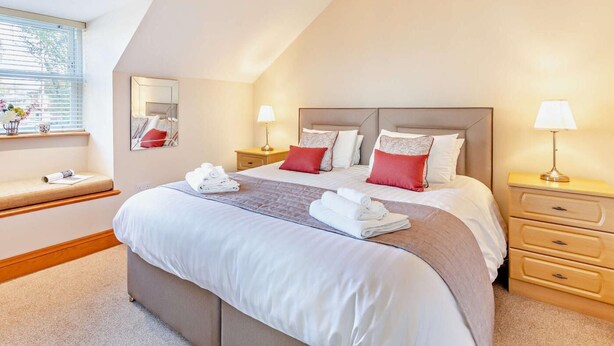 A bedroom with a large bed, two bedside tables with lamps, a window with blinds, a bedside table with a vase, and a mirror on the wall. - 1 Bed in Alnwick (oc-cn215) (Alnwick)