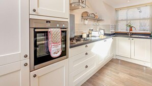 A modern kitchen with white cabinetry, a stainless steel oven, a built-in range hood, and a window with blinds. - 1 Bed in Alnwick (oc-cn215) (Alnwick)