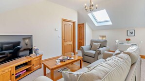 A modern living room with a flat-screen TV, wooden entertainment unit, sofa, and a dining area with a table and chairs. - 1 Bed in Alnwick (oc-cn215) (Alnwick)