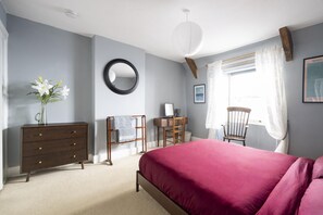 Quarto com cama, penteadeira, cadeira, escrivaninha e janela com cortinas.