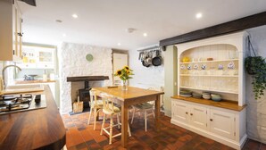 A kitchen with a wooden table, white cabinets, and a stone wall. - 2 Bed in Bideford (oc-59434) (Appledore)