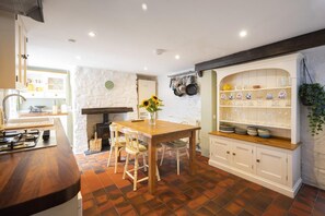 A kitchen with a wooden table, white cabinets, and a stone wall. - 2 Bed in Bideford (oc-59434) (Appledore)