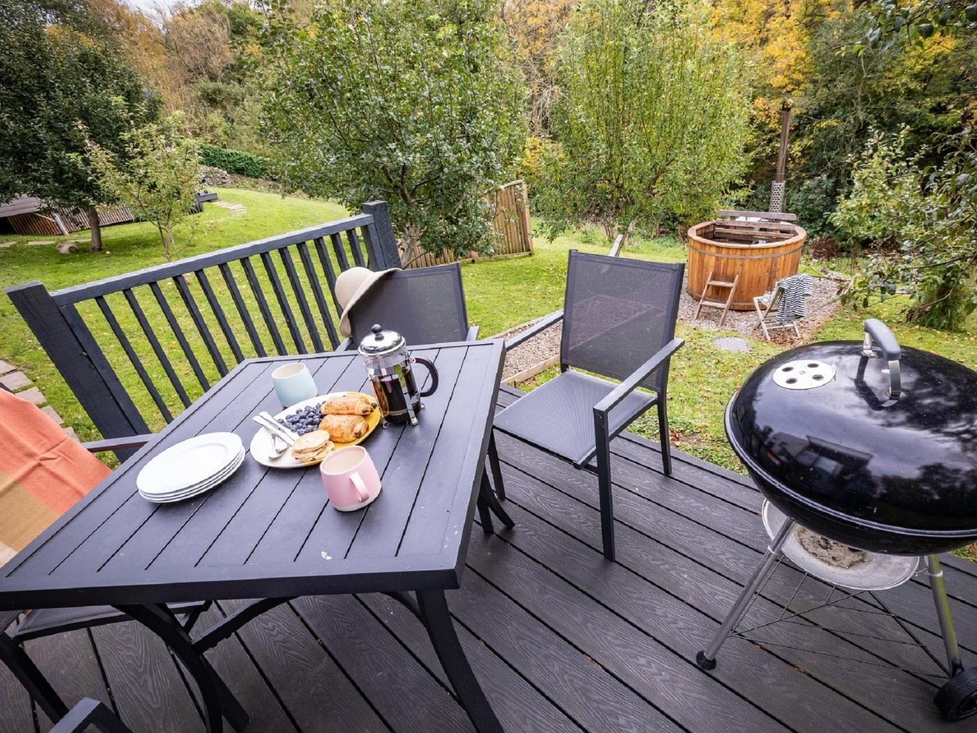 A deck with a table set for breakfast, a grill, and a wooden bench.