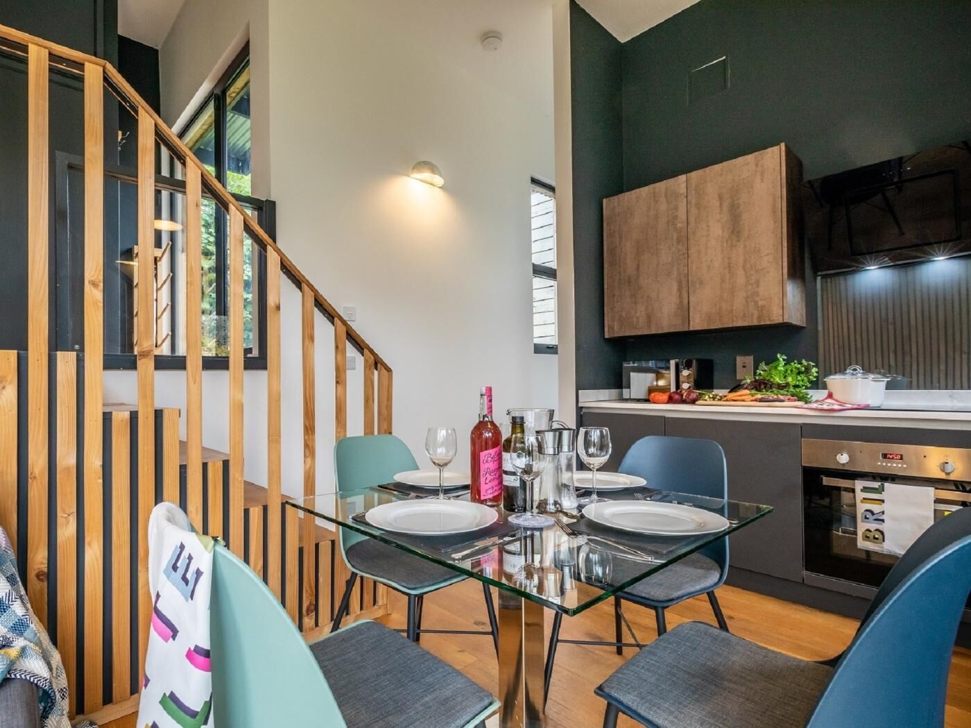 Een moderne keuken met een eethoek, een houten trap en uitzicht op groen.
