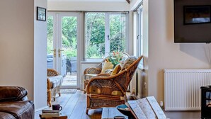 Een woonkamer met rieten meubels, een leren bank, een televisie en uitzicht op groen.
