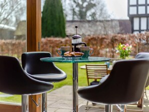 A patio with a glass table, two black chairs, a coffee maker, and a cup of coffee. - 2 Bed in Ludlow (oc-59293) (Richards Castle)