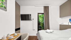 A hotel room with a bed, a desk with a tray of breakfast items, a TV mounted on the wall, and a window with a view of greenery. - Pure Bliss Villa With Jacuzzi (Tisno)