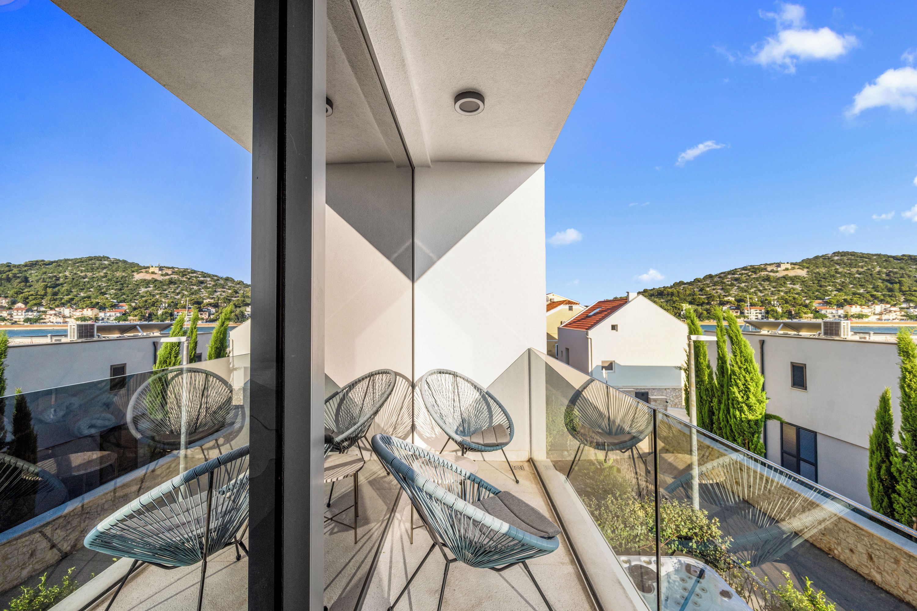 A balcony with a glass railing, wicker chairs, and a view of a hilly landscape.