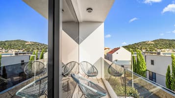 A balcony with a glass railing, wicker chairs, and a view of a hilly landscape.
