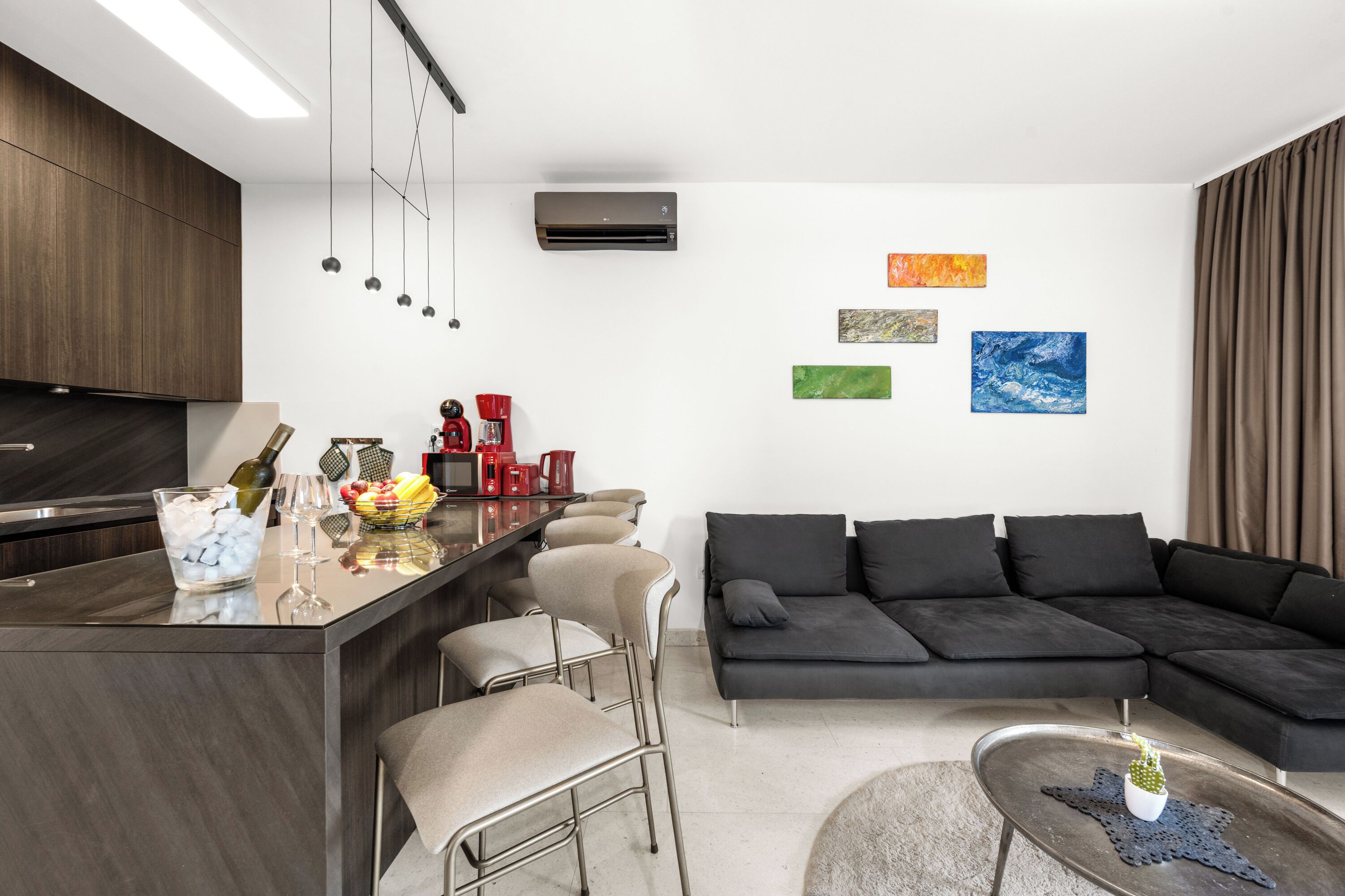 A modern kitchen with a bar area, a black sectional sofa, and artwork on the walls.