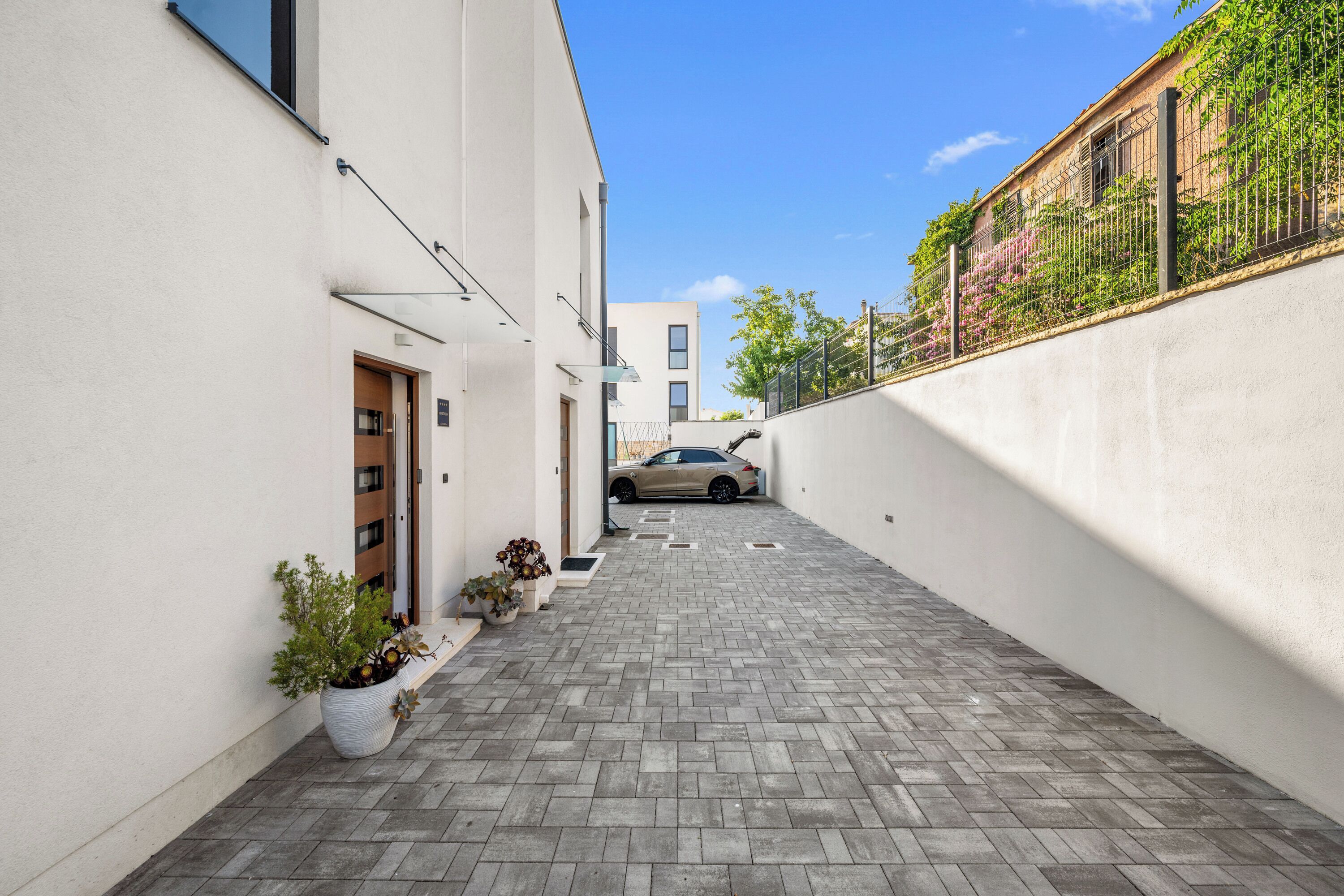 A narrow alleyway with a paved walkway, potted plants, and a parked car.