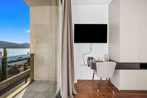 A modern room with a balcony overlooking a body of water, a flat-screen TV mounted on the wall, a desk with a chair, and a wooden floor. - Pure Bliss Villa With Jacuzzi (Tisno)