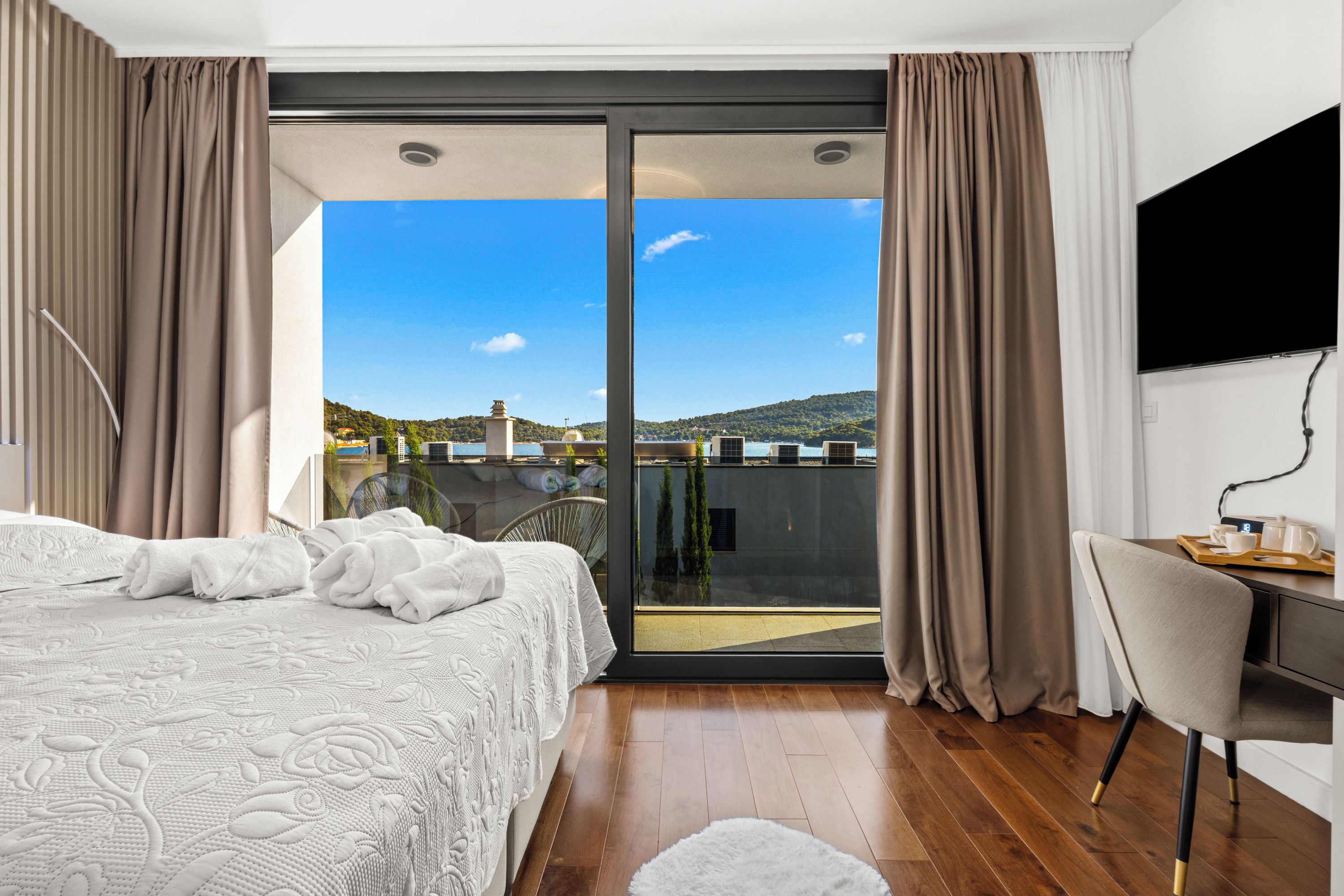 A bedroom with a bed, a desk, and a view of a balcony.