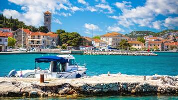A coastal town with a clear blue sea, a stone pier, and buildings with red-tiled roofs.