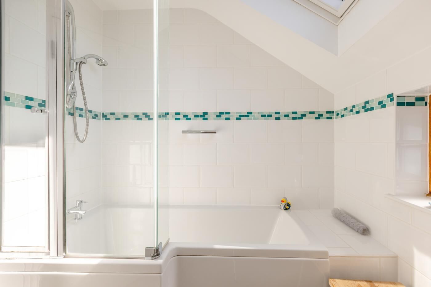 A modern bathroom with a glass shower enclosure, a bathtub, and a small window.