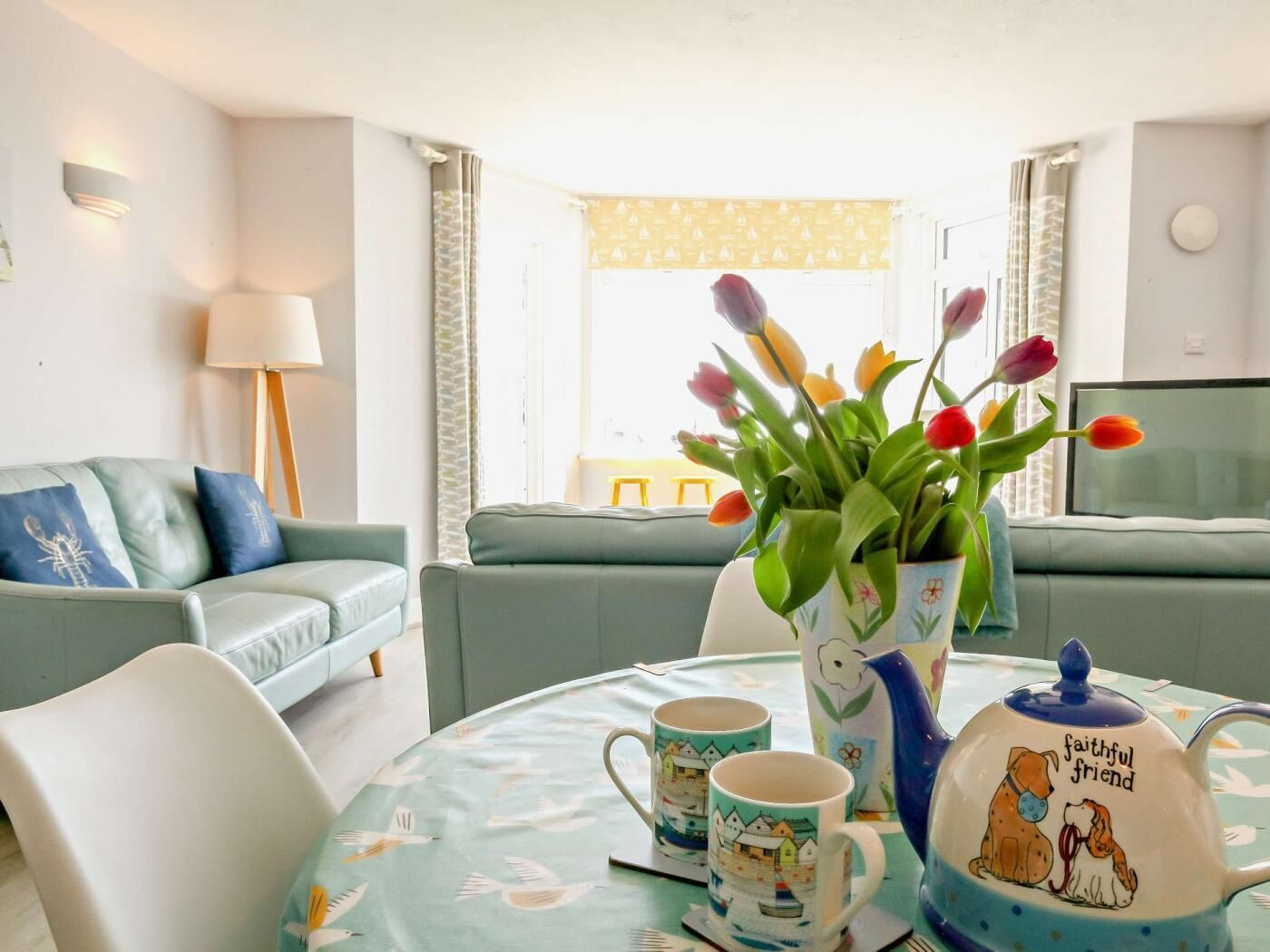 A living room with a sofa, a table with a teapot and cups, and a vase with tulips.