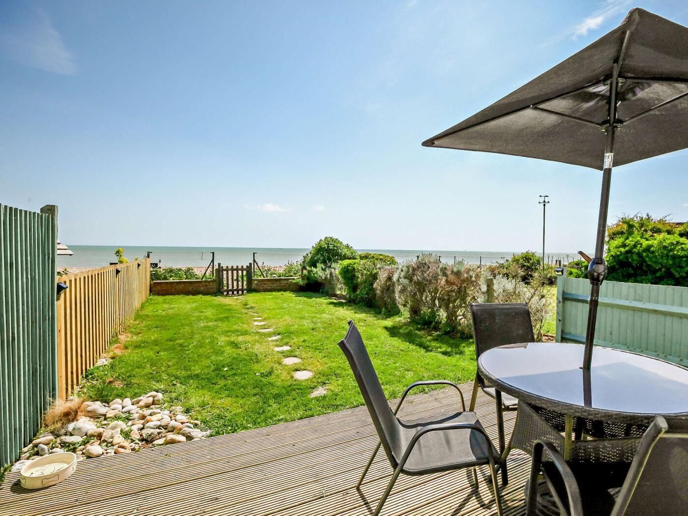 A patio with a table and chairs, a small garden, and a view of the sea.