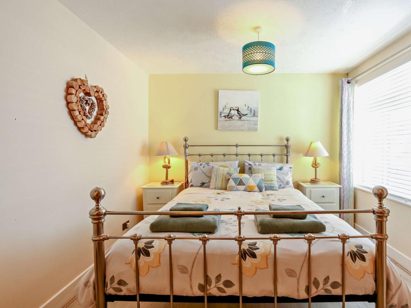 A bed with a metal frame, two bedside tables, a wall-mounted lamp, and a picture on the wall.