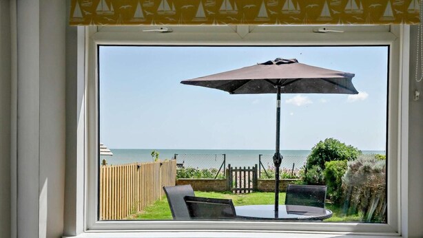 Ein Zimmer mit einem großen Fenster, einem Tisch mit Sonnenschirm und zwei gelben Hocker.