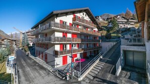 Et hotel med flere etager, med altaner, en trappe og udsigt til det omkringliggende bjerrelandskab.