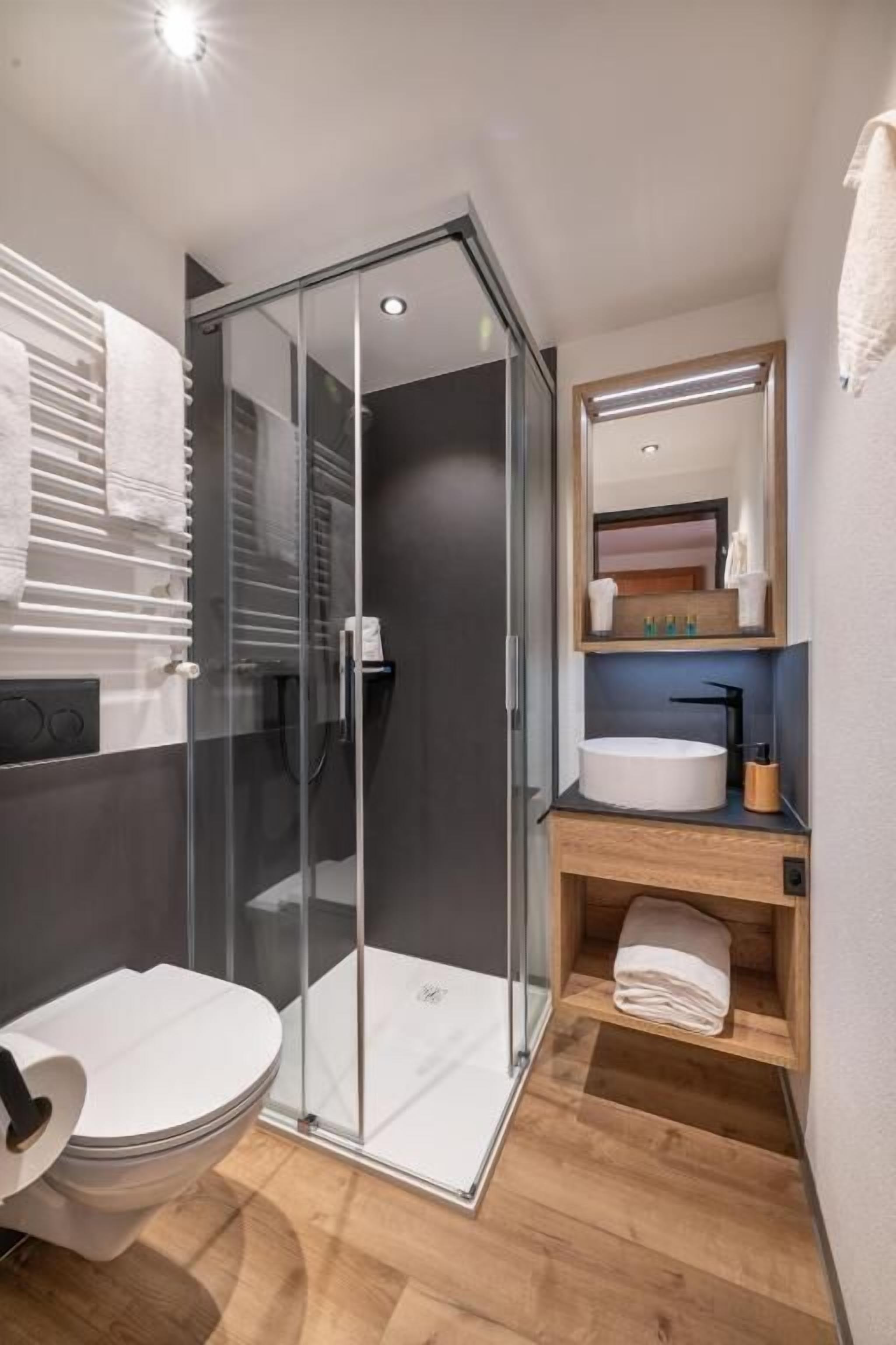 A modern bathroom with a glass shower enclosure, a toilet, a sink with a mirror, and a wooden vanity.