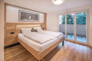 A double bed with a wooden headboard, a framed picture above, and a large window with blinds. - Haus Juliana Alpenrose (Zermatt)