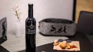 En flaske Tenud vin på et bord med en underlag, en grå dekorativ skål og en lille tallerken med snacks.