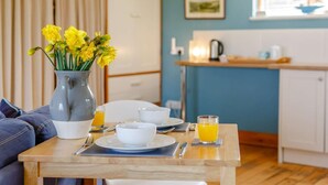 A dining area with a table set for breakfast, a vase of flowers, and a kitchen in the background. - 1 Bed in Alnwick (oc-cn212) (Bilton)