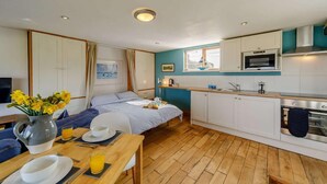 A compact room with a bed, a dining table with breakfast items, a kitchenette with modern appliances, and a window with a view. - 1 Bed in Alnwick (oc-cn212) (Bilton)