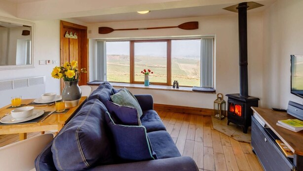 A living room with a sofa, a dining table with breakfast items, a large window with a view, and a wood-burning stove. - 1 Bed in Alnwick (oc-cn212) (Bilton)