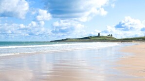 Ein Strand mit einer grasbewachsenen Hügel und einer entfernten, schlossähnlichen Struktur.