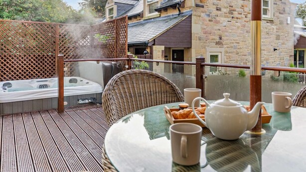 Ein Whirlpool auf einer Holzterrasse mit Korbstühlen und einem Tisch, gedeckt für Tee.