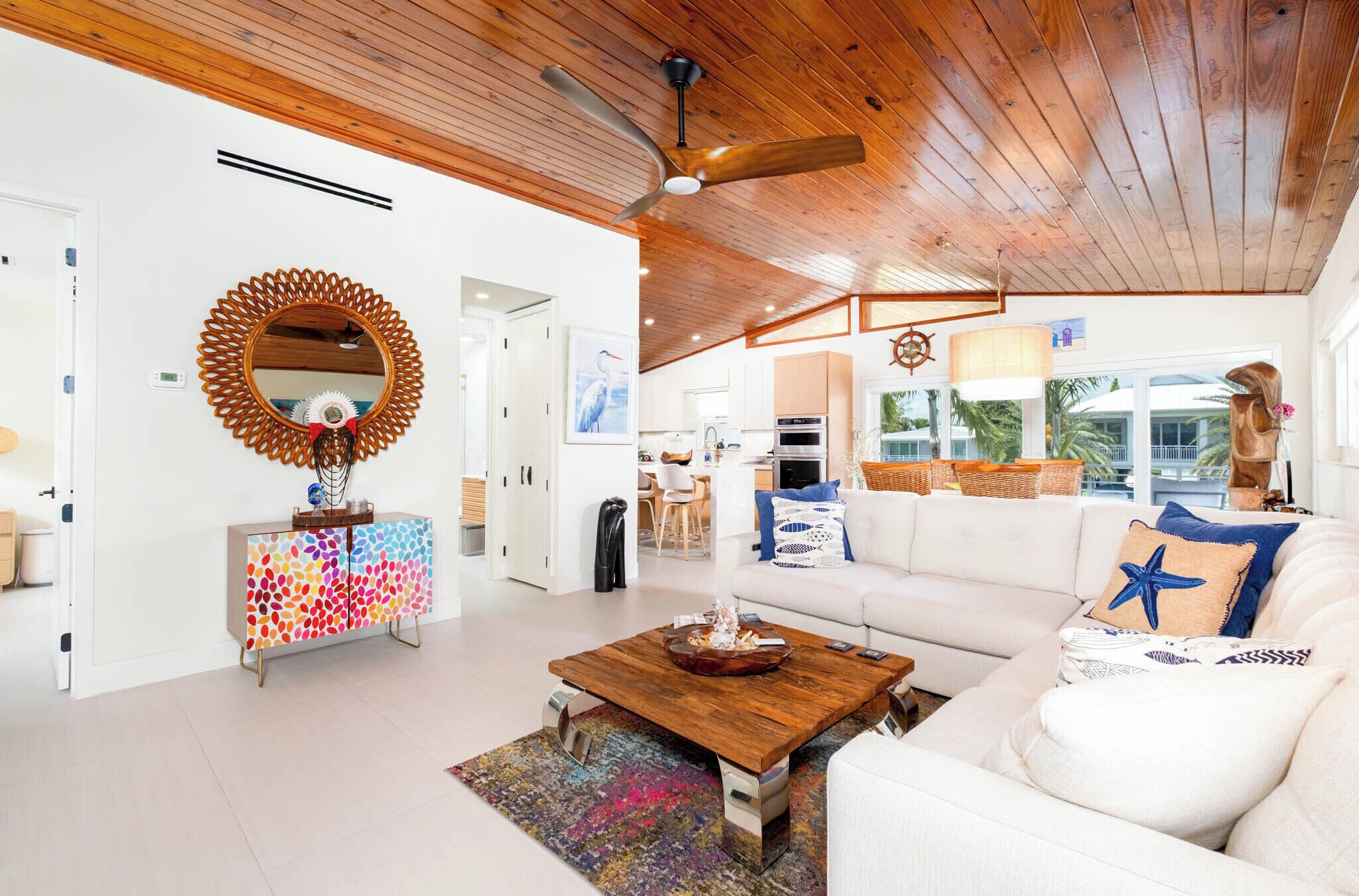 A modern living room with a wooden ceiling, a white sofa, a colorful cabinet, and a large mirror.