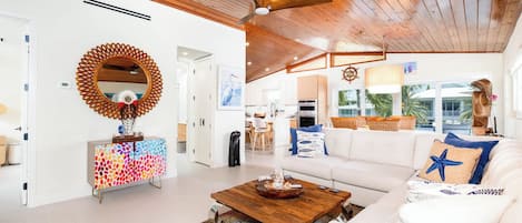Una sala de estar moderna con techo de madera, un sofá blanco, un mueble de colores y un espejo grande.
